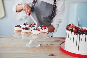 Close up view of woman that makes slices of the cookies by using knife in the kitchen with pie on the table photo