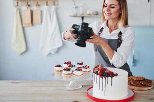 la mujer se para en la cocina y toma una foto de sus galletas caseras y su pastel usando una cámara