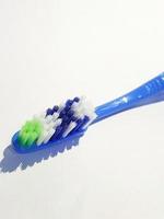 Isolated white photo of a plastic toothbrush that has been used several times. This toothbrush has a blue handle.