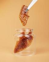 glass jar with brown cannabis wax, pieces of hardened resin of marijuana extract on an orange background photo