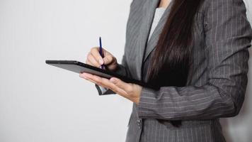 Asian businesswoman working at home using tablet device, browsing internet playing social media in video call meeting with colleagues and coworkers planning innovative ideas, quarantine self-isolation photo