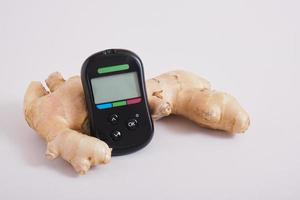 glucose meter monitor and ginger root on gray background photo