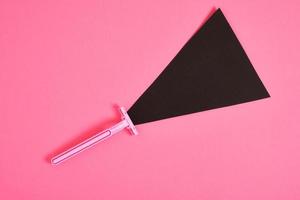 pink plastic disposable razor and black paper triangle on pink background photo