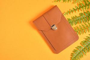 phone and wallet bag and fern on orange background, eeo vegan leather from plants concept copy space photo