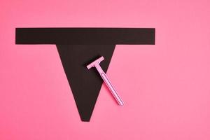 pink plastic disposable razor and black paper triangle on pink background photo