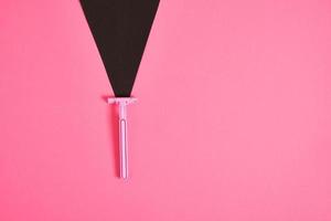 pink plastic disposable razor and black paper triangle on pink background photo