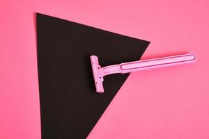 pink plastic disposable razor and black paper triangle on pink background photo
