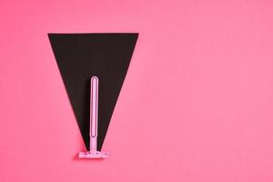 pink plastic disposable razor and black paper triangle on pink background photo