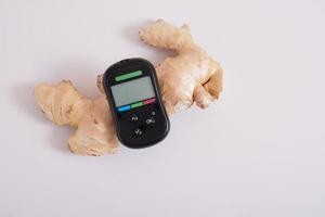 glucose meter monitor and ginger root on gray background photo