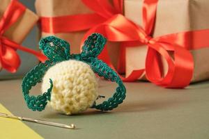 crochet hook, handmade knitted ball for christmas and gift boxes with red ribbons on a green background photo