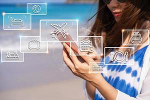 Young Asian woman traveler using her smartphone at a tropical sandy beach for finding information and planning trip, Summer vacation concept photo