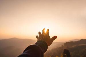 mano de hombre joven alcanzando las montañas durante la puesta de sol y el hermoso paisaje foto