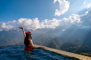Young woman traveler relaxing in sky pool and looking at the beautiful nature landscape with blue sky and a sunbeam in Sapa, Vietnam photo