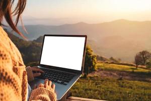 joven viajera independiente que trabaja en línea usando una computadora portátil y disfrutando del hermoso paisaje natural con vista a la montaña al amanecer foto