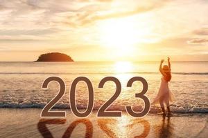 Young woman traveler looking beautiful sunset on the tranquil beach celebrating New Year 2023, Summer vacation concept photo