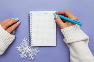 Woman hand with winter nails holding pen on notebook and writing wish list photo