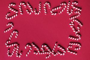 Flat lay Christmas composition with frame of candy canes on a red background. Copy space for text photo