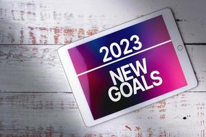 Top view of white wood desk with digital tablet and new goals text on screen with copy space. Planning new goals to reach this next year. Achievements, aspirations and wishes. photo