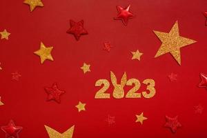 2023 new year flat lay concept with rabbit. Numbers 2023 with red and gold stars, top view on red background photo