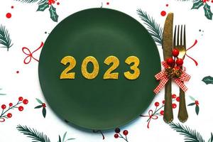 Happy new year 2023. Top view of golden Numbers 2023 on plate with cutlery for Christmas dinner. New Years Eve celebration concept background