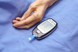 Hand of elderly woman and blood sugar monitor on blue background. Health and physical examination concept. photo