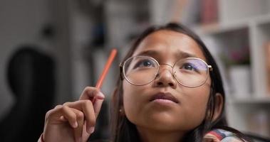 Closeup of Young asian active girl glasses thinking while sitting at desk at classroom. Education concept.