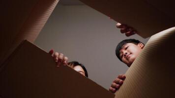 Inside of package view, slow motion shot, Happy young couple opens package and grabbing books from cardboard box, New house concept. video