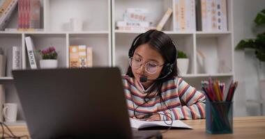 porträtt av flicka glasögon med hörlurar inlärning uppkopplad uppkopplad via bärbar dator medan Sammanträde på skrivbord på Hem. ung kvinna skrivning på bok. utbildning och e-learning begrepp. video