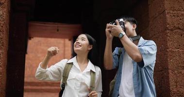 contento asiatico viaggiatore coppia con cappello prende un' foto e visite antico tempio. sorridente giovane uomo e donna in piedi e guardare antico tempio. vacanza, viaggio e passatempo concetto. video