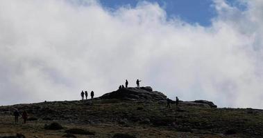 silhuetas de turistas admirando a vista no topo da serra da estrela, a montanha mais alta de portugal continental com nuvens espessas ao redor. viajar e explorar. pessoas no pico da montanha. video