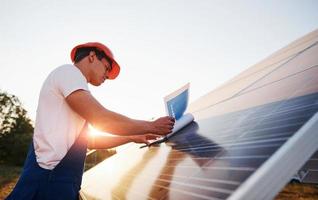 Beautiful sunlight. Male worker in blue uniform outdoors with solar batteries photo