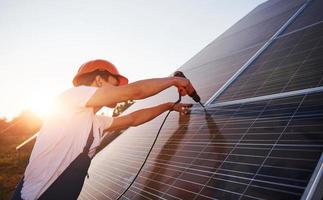 utilizando un destornillador inalámbrico. trabajador masculino en uniforme azul al aire libre con baterías solares en un día soleado foto