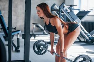 Young fitness woman with slim type of body doing exercises by using barbell photo