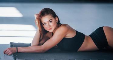 Young woman with slim type of body and in black sportive clothes lying down on the fitness mat photo