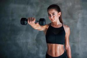 Young fitness woman is in the gym near wall with dumbbells in hands photo