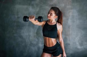 Young fitness woman is in the gym near wall with dumbbells in hands