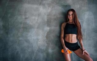 Young fitness woman with slim type of body and bottle of water is leaning on the wall photo