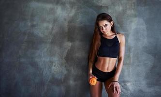 Young fitness woman with slim type of body and bottle of water is leaning on the wall photo