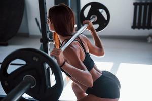 Young fitness woman with slim type of body doing exercises by using barbell photo