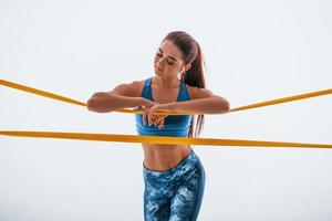 Leaning on yellow resistance band. Young woman with slim body type isolated against white background photo