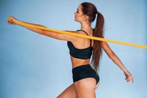 Hands exercise by using resistance band. Young woman with slim body type isolated against blue background photo