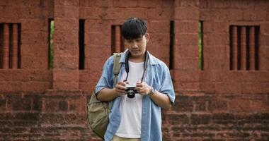 Portrait of Happy asian traveler man with hat taking a photo and looking at camera at ancient temple. Smiling young male standing and holding camera. Holiday, travel and hobby concept. video