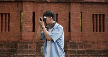 portret van gelukkig Aziatisch reiziger Mens met hoed nemen een foto en op zoek Bij camera Bij oude tempel. glimlachen jong mannetje staand en Holding camera. vakantie, reizen en hobby concept. video