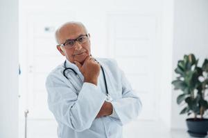 Portrait of senior doctor in white uniform that stands in the clinic photo