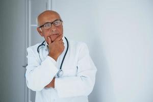 Portrait of senior doctor in white uniform that stands in the clinic photo