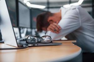 hombre de negocios cansado durmiendo en el lugar de trabajo apoyándose en la mesa con múltiples pantallas. información bursátil en pantallas foto