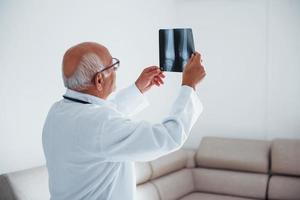 médico senior en uniforme blanco examina la radiografía de las piernas humanas foto