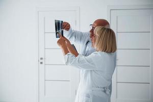 Senior man and woman doctors in white uniform examines x-ray of human legs photo