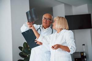 Senior man and woman doctors in white uniform examines x-ray of human legs photo