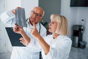 Senior man and woman doctors in white uniform examines x-ray of human legs photo